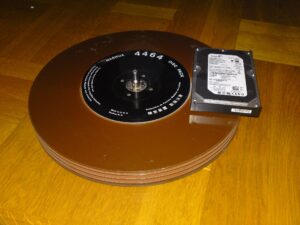 Platters of a 14" Nashua hard disk pack from the 1970s featured next to a 3.5" hard drive from a desktop computer to demonstrate the size of disk packs.
